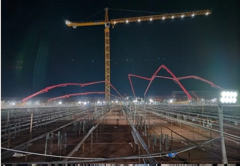 Night shot of a tower crane and concrete pump booms over a rebar site