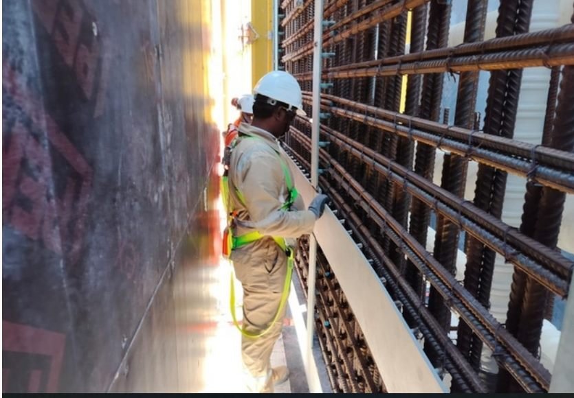 Worker in safety harness inspecting formwork on a tank wall