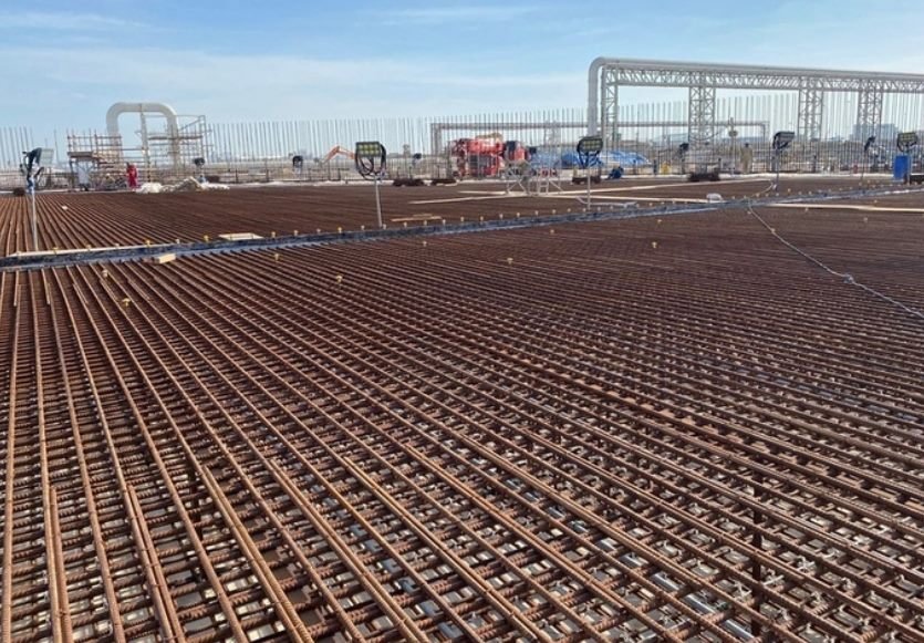 Wide daytime view of a large rebar mat with a structural steel gantry