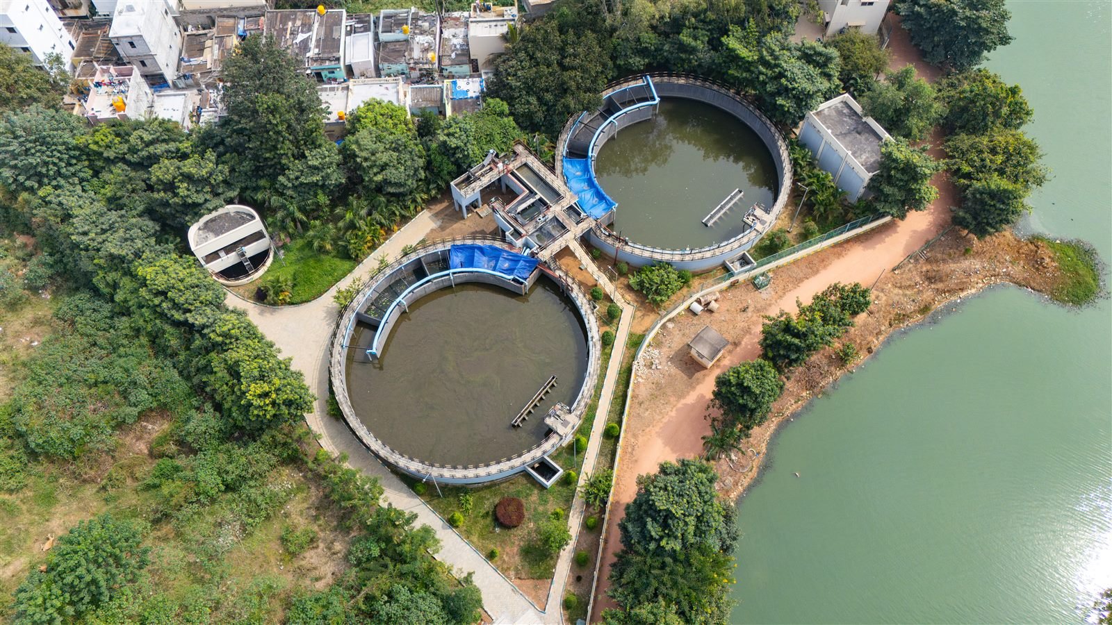 Aerial view of circular wastewater treatment clarifier tanks beside a lake
